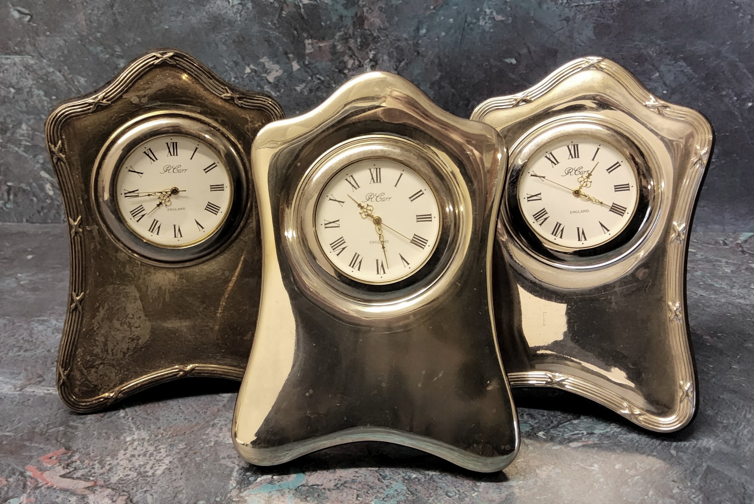 Two silver mounted miniature clocks in form of a shaped mantel clock, wood backed, an embosed and