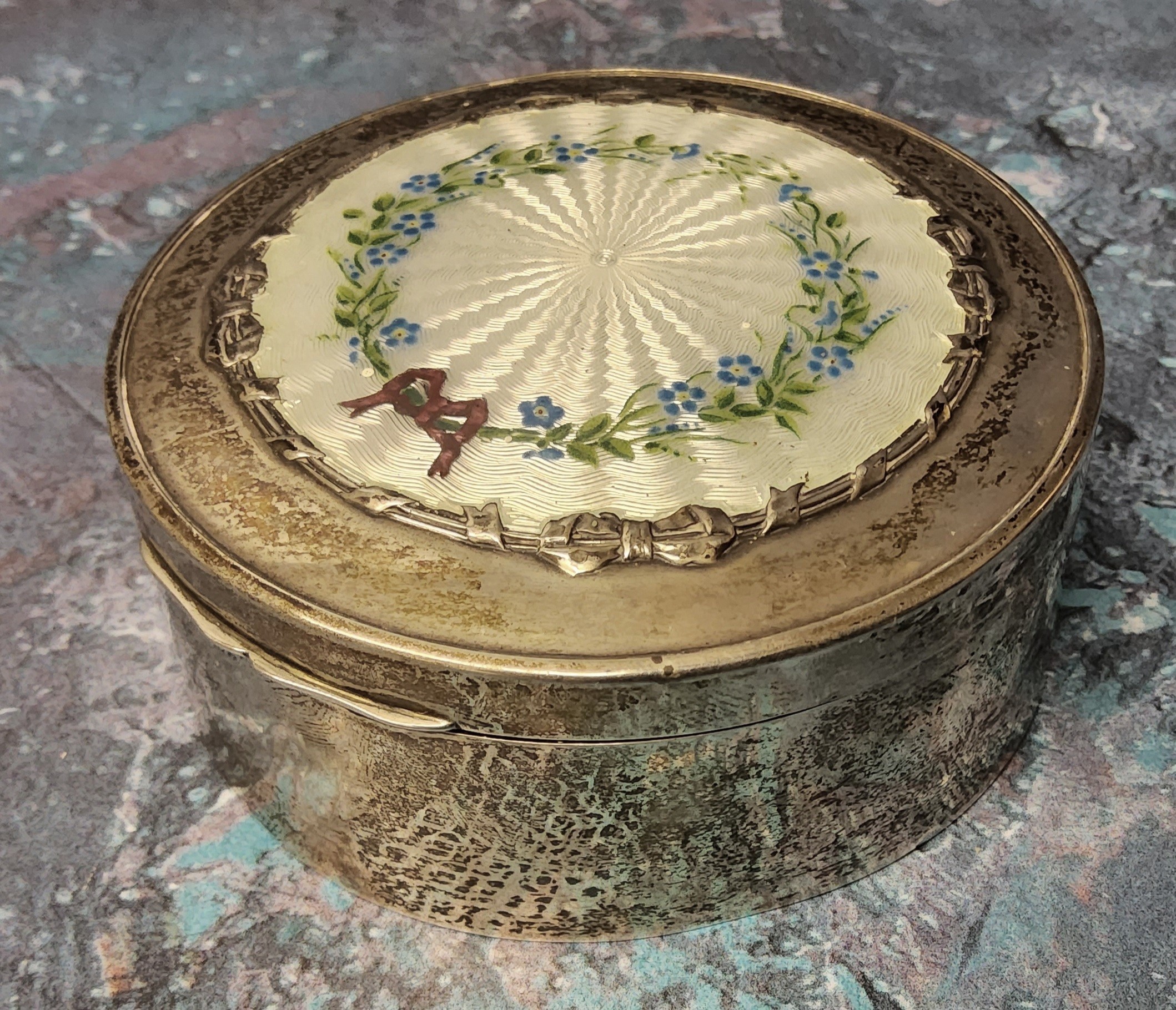 A silver circular jewellery trinket box, the hinged cover decorated with a central white guilloche