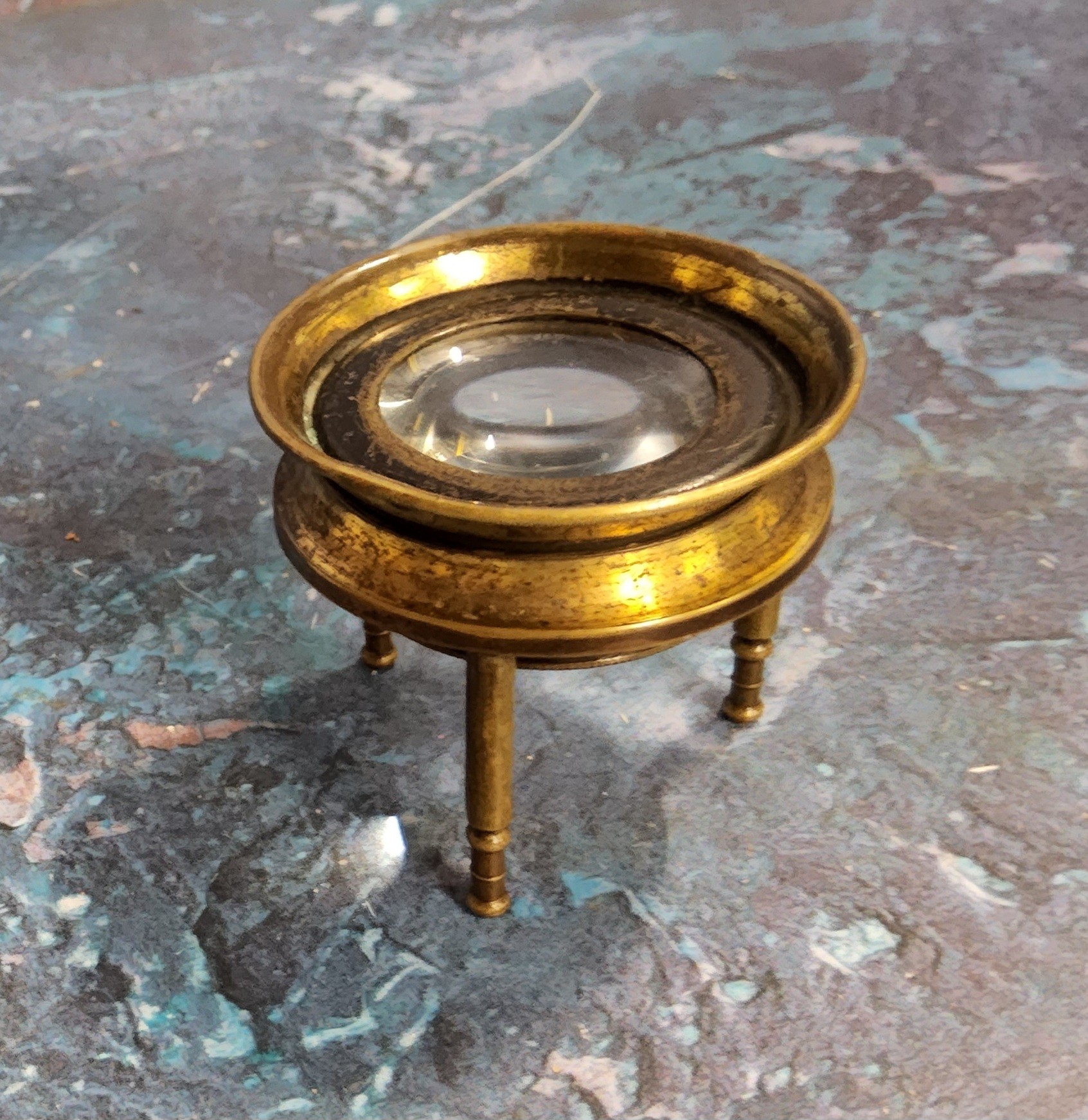 A Victorian brass map magnifying loupe raised on three shaped legs, adjustable magnifying lens