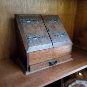 An Arts and Crafts oak slope front stationery box, the interior with waterfall letter rack, drawer