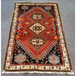 A woollen rug, with three lozenges and roundels to angles, in cream, blue and and orange on a red