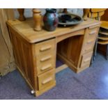 A light oak knee hole desk, central blind drawer to frieze flanked by slide-outs above four drawers,