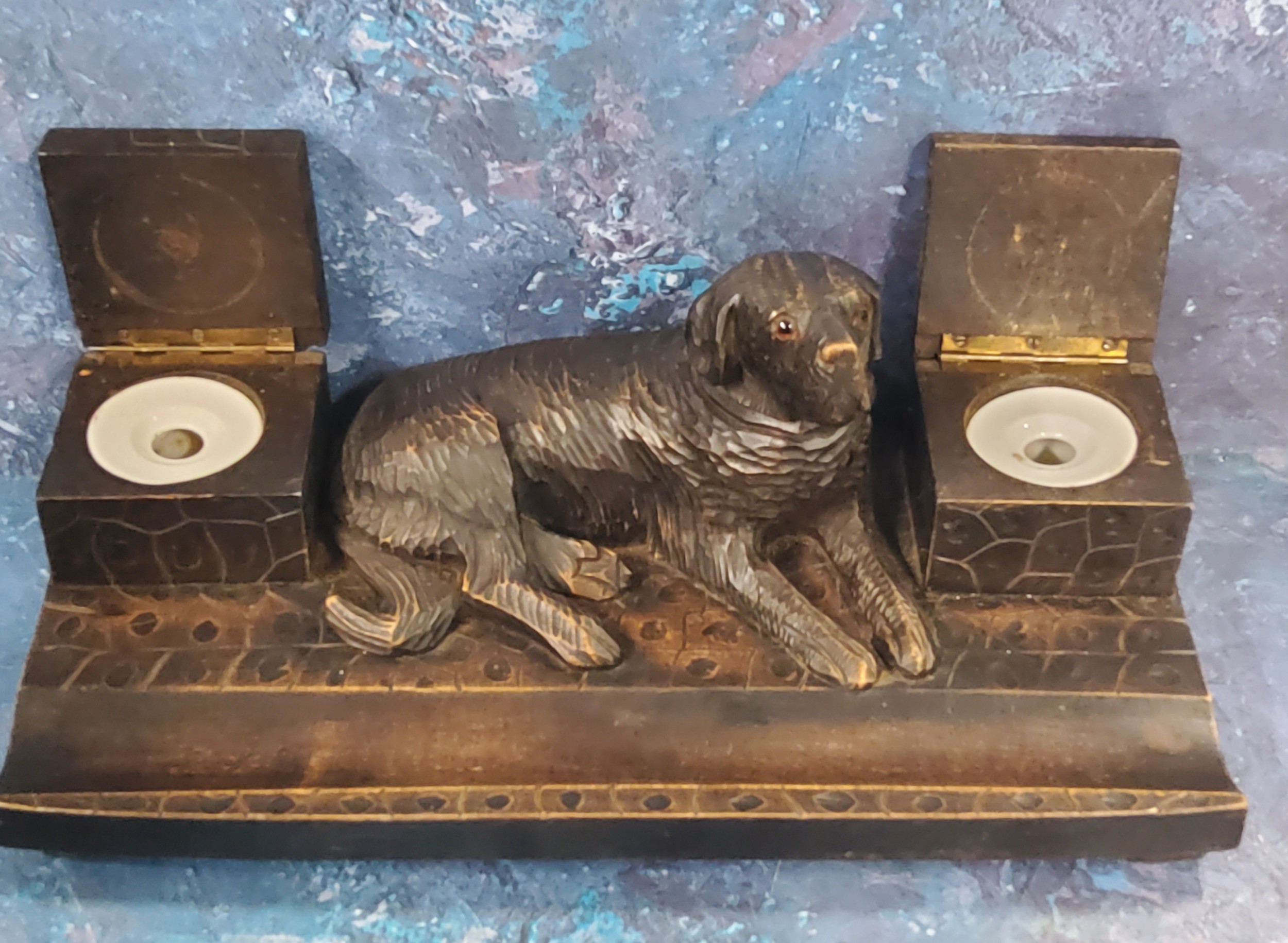 A 19th century Black Forest standish, carved with a large dog reclining between two square covered