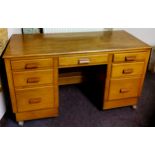 An early 20th century teak kneehole desk with butterscotch amber Bakelite handles, castors.