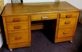 An early 20th century teak kneehole desk with butterscotch amber Bakelite handles, castors.