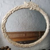 A substantial oval mirror, painted in off white surmounted with flowers and swags.