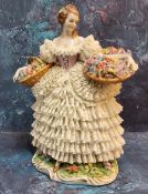 A Sitzendorf lace figure, of a Flower Lady, she stands holding with two baskets, her skirt from