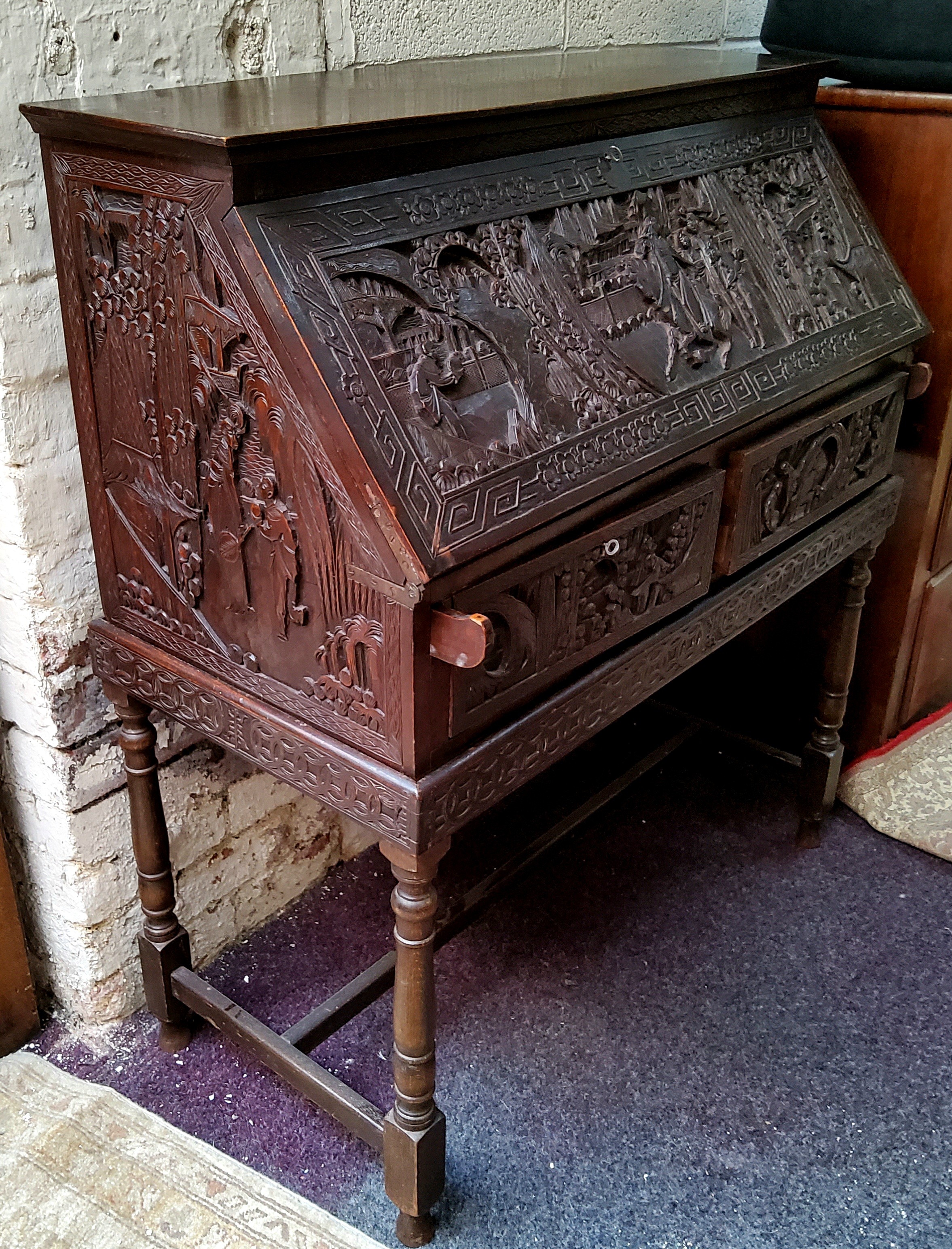 A late 19th / early 20th century carved padouk wood scholar's bureau on stand, profusely carved with