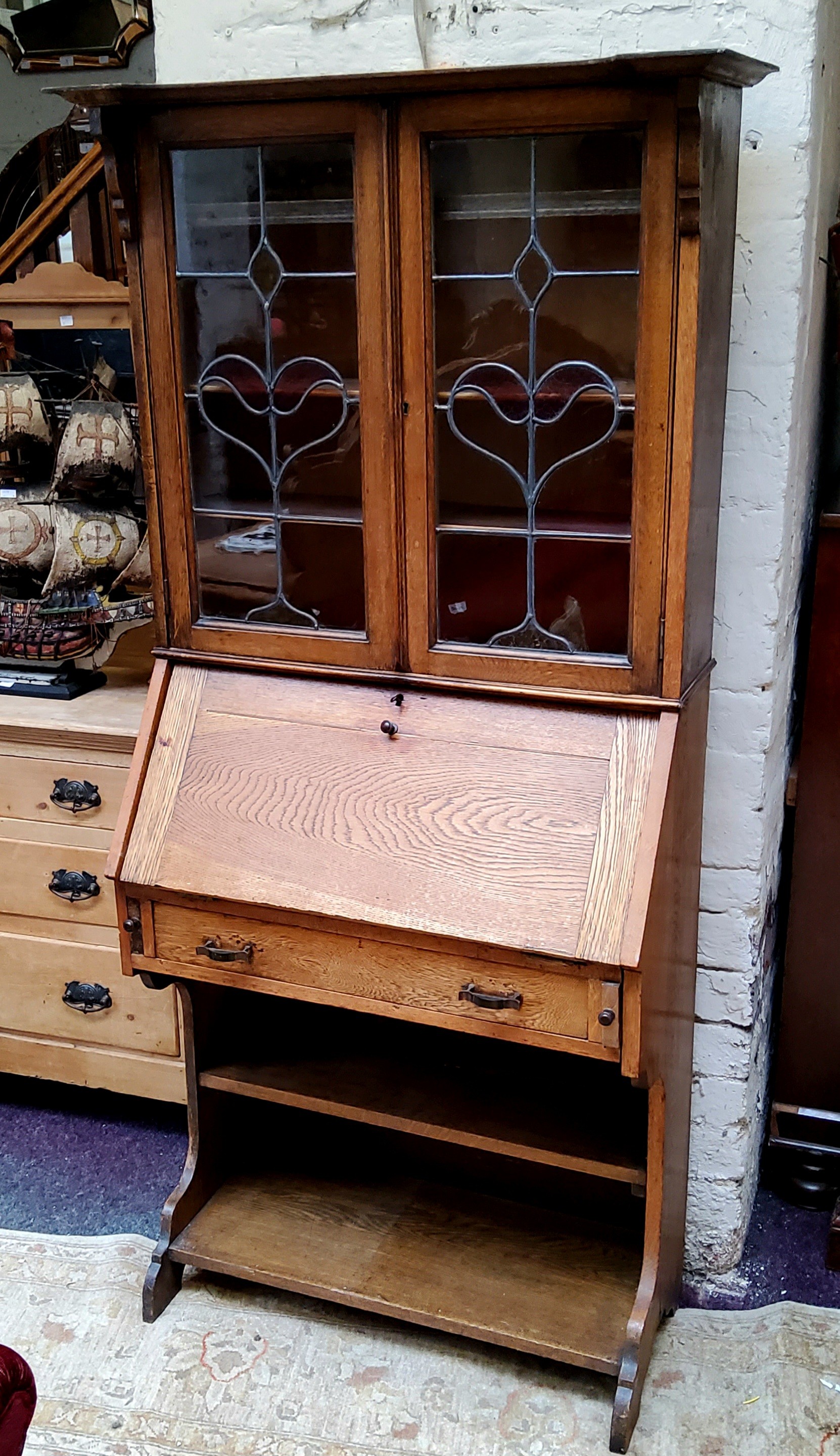 An Arts & Crafts oak bureau bookcase with oversailing cornice, sinuous stained glass leaded panel