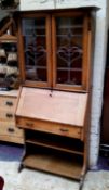 An Arts & Crafts oak bureau bookcase with oversailing cornice, sinuous stained glass leaded panel
