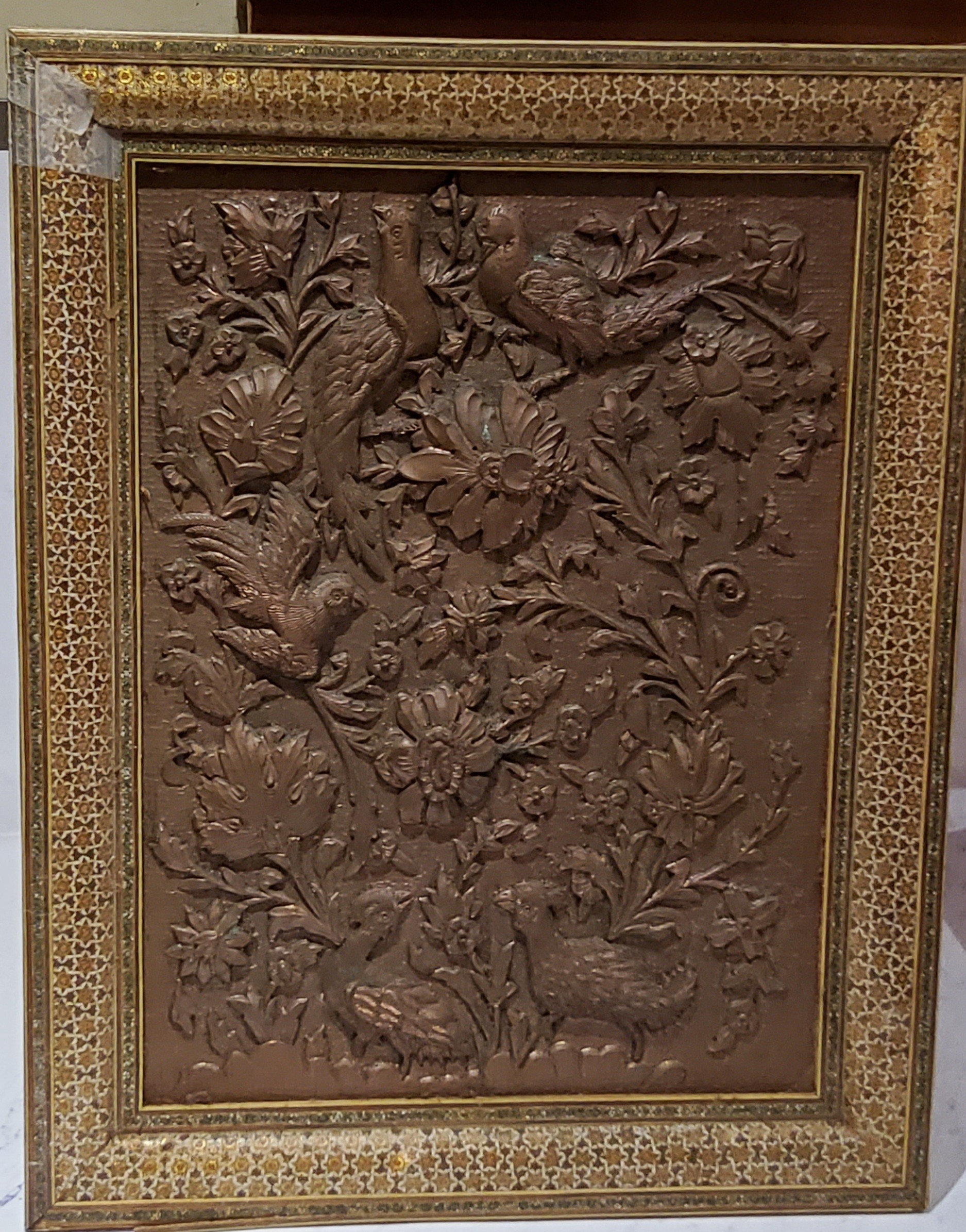 An Islamic copper panel, embossed with birds and foliage, Kahatan marquetry frame, 49cm x 39cm