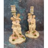 A pair of German figural candlesticks, of a maiden and cherub, floral encrusted bases, 31cm high,