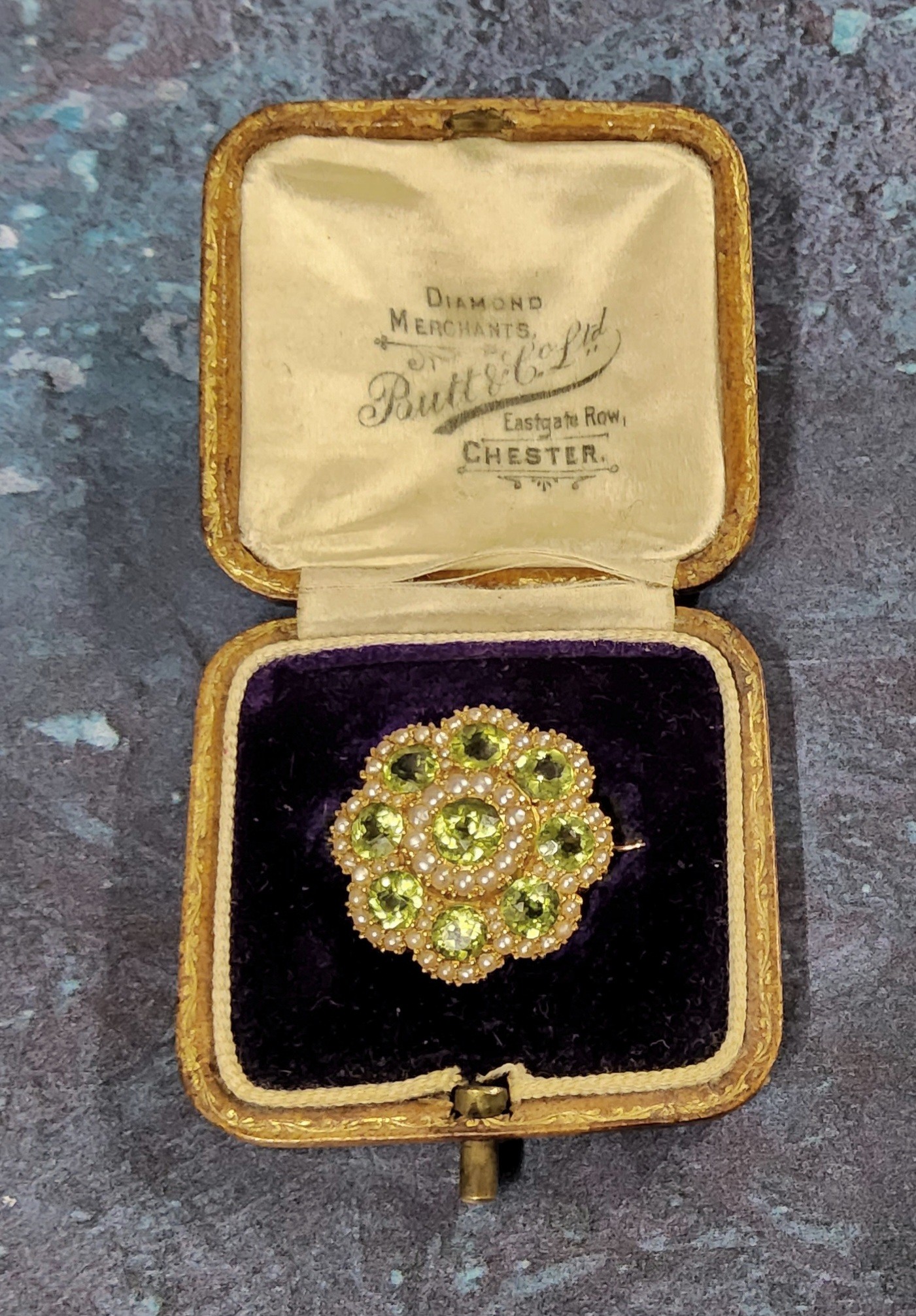 An unusual yellow brooch in the form of a flower head, set with nine round peridots and seed pearls,