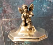 A sterling silver menu holder, as a cherub, seated, spreading square base, 4.25cm wide, marks rubbed