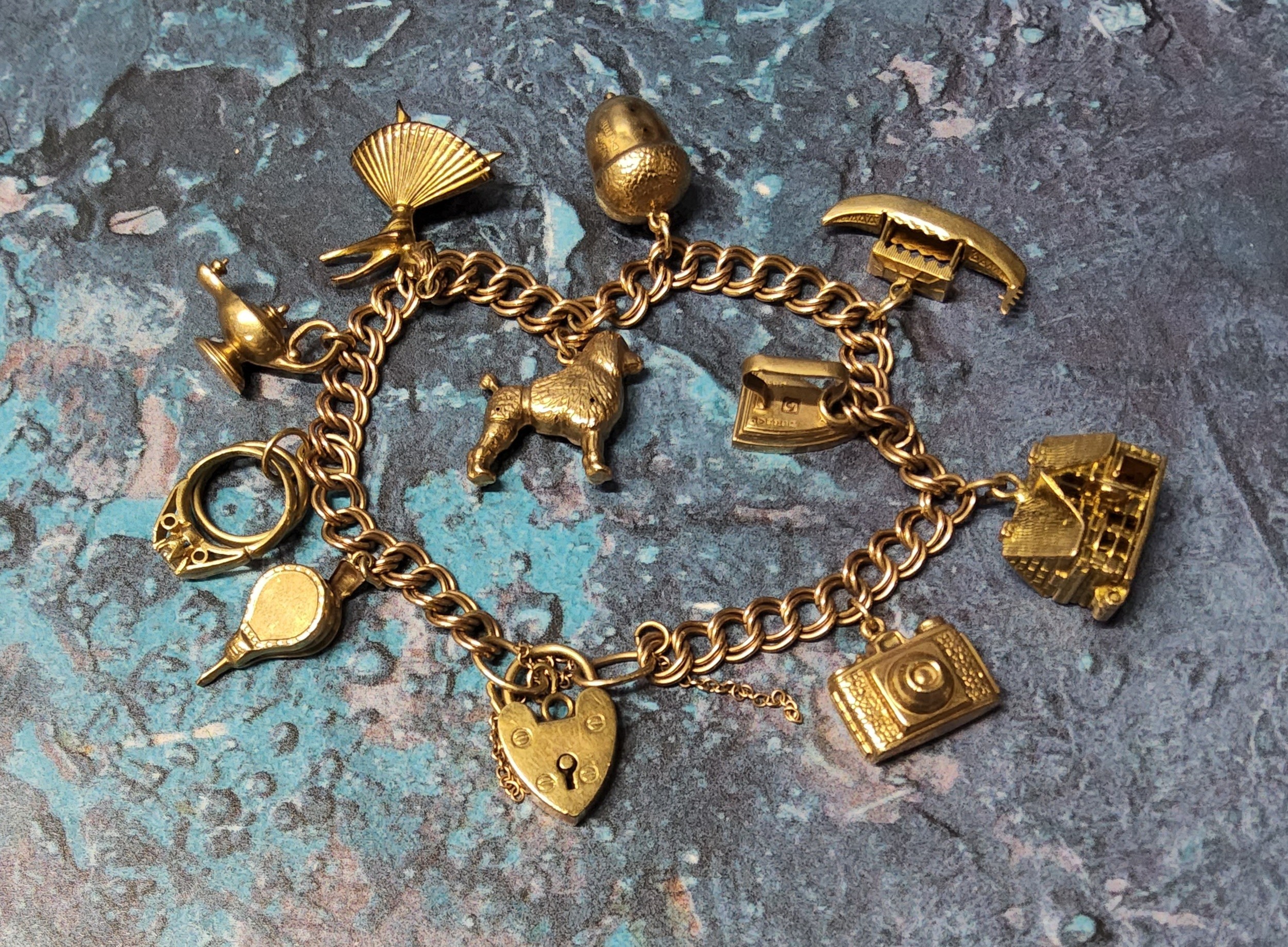 A 9ct gold charm bracelet with ten 9ct gold charms including a hinged pub, camera, poodle etc, 9ct