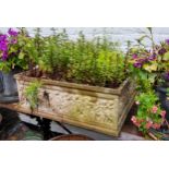 A large square reconstituted stone planter, decorated in relief with putti figures, with herbs