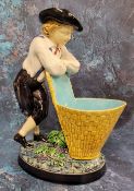 A Minton majolica figure, The Grape Picker, he stands leaning on his pannier, 24cm high, impressed