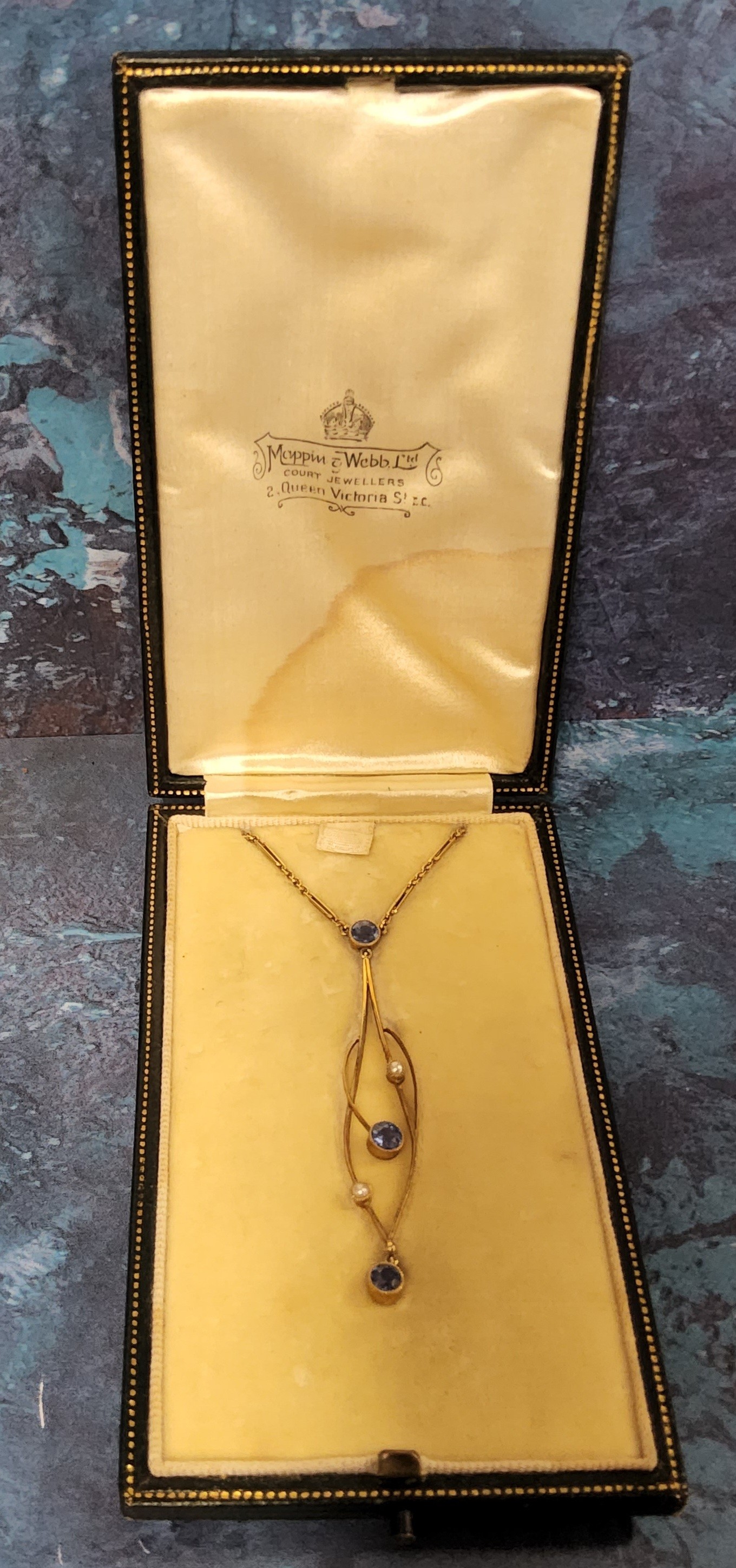 An Art Nouveau yellow metal, sapphire & seed pearl drop pendant of sinuous form, collet set with