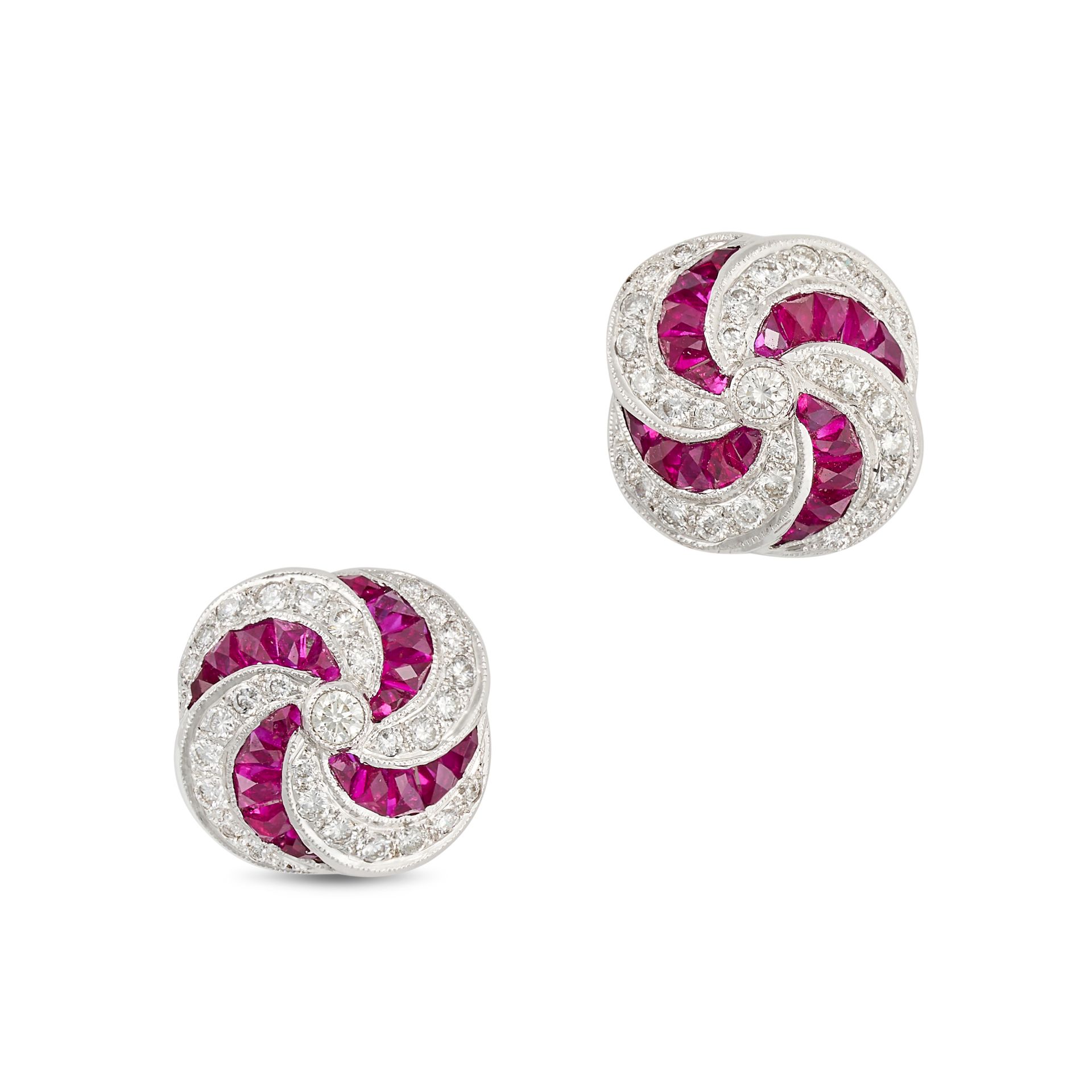 A PAIR OF RUBY AND DIAMOND EARRINGS in 18ct white gold, each stud in a scrolling design, set with...