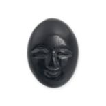 AN UNMOUNTED CARVED ONYX oval shaped, with a stylised smiling face carved on the concave side, 23...