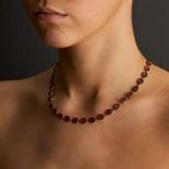AN ANTIQUE GARNET RIVIERE NECKLACE in yellow gold, set with a row of oval cut garnets, stamped 9K...