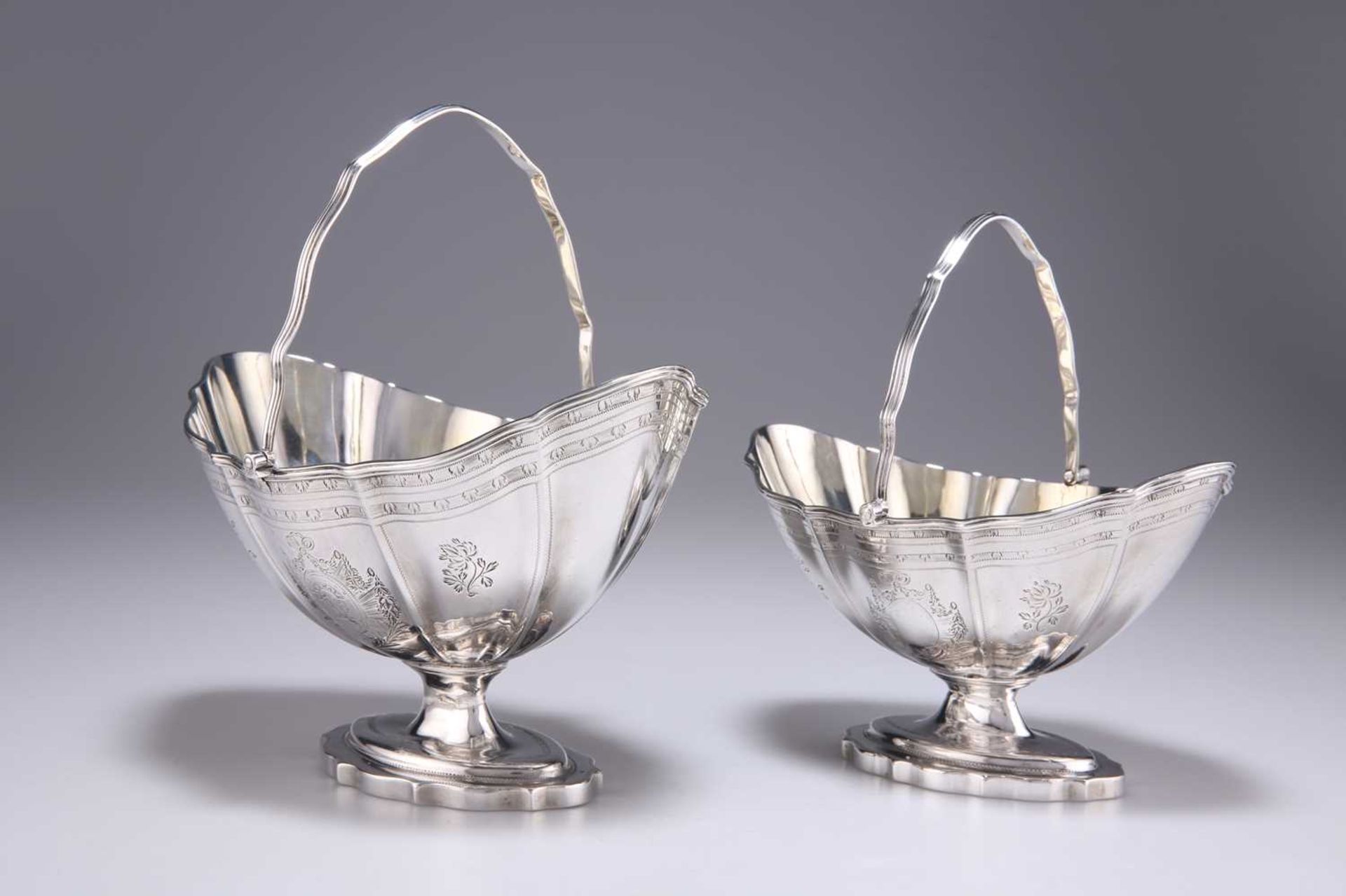 A GRADUATED PAIR OF GEORGE III SILVER SWING-HANDLED SUGAR BASKETS