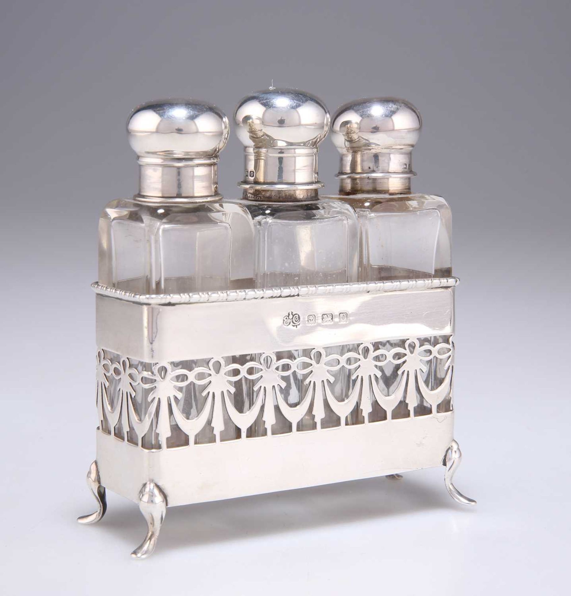 A GEORGE V SILVER SET OF THREE SILVER-TOPPED GLASS SCENT BOTTLES IN A SILVER STAND