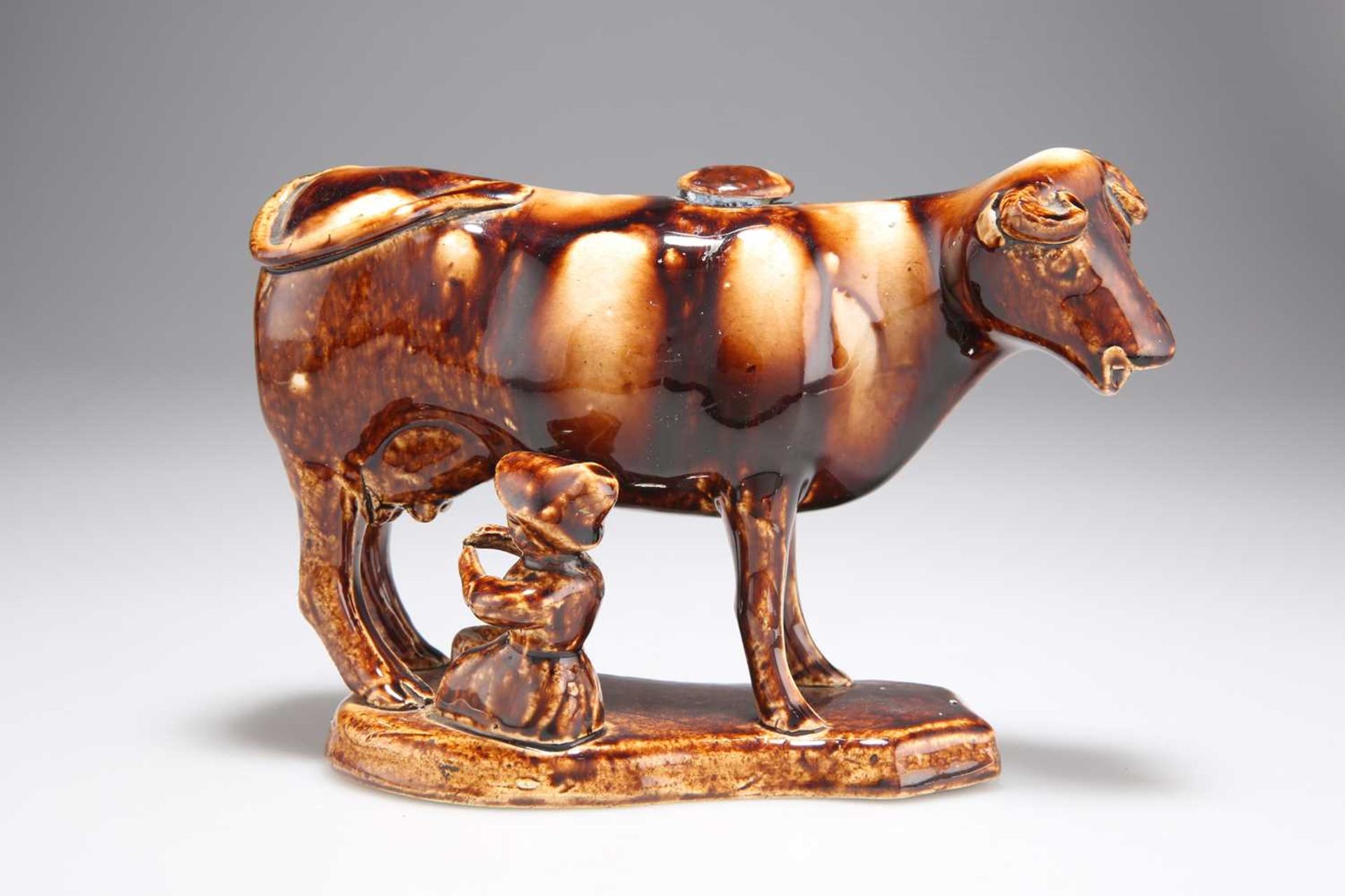 A 19TH CENTURY STAFFORDSHIRE TREACLE-GLAZED POTTERY COW CREAMER AND MILKMAID GROUP