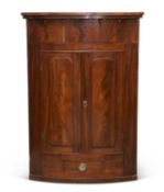 A LARGE REGENCY MAHOGANY BOW-FRONT HANGING CORNER CUPBOARD
