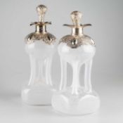 A PAIR OF EDWARDIAN SILVER-MOUNTED GLASS 'GLUG GLUG' DECANTERS AND STOPPERS