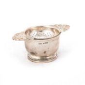 A GEORGE VI SILVER TEA STRAINER ON STAND