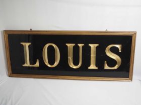 A framed and glazed sign reading 'Louis', 154cmx60cmx4cm crack in right hand side of glass. This