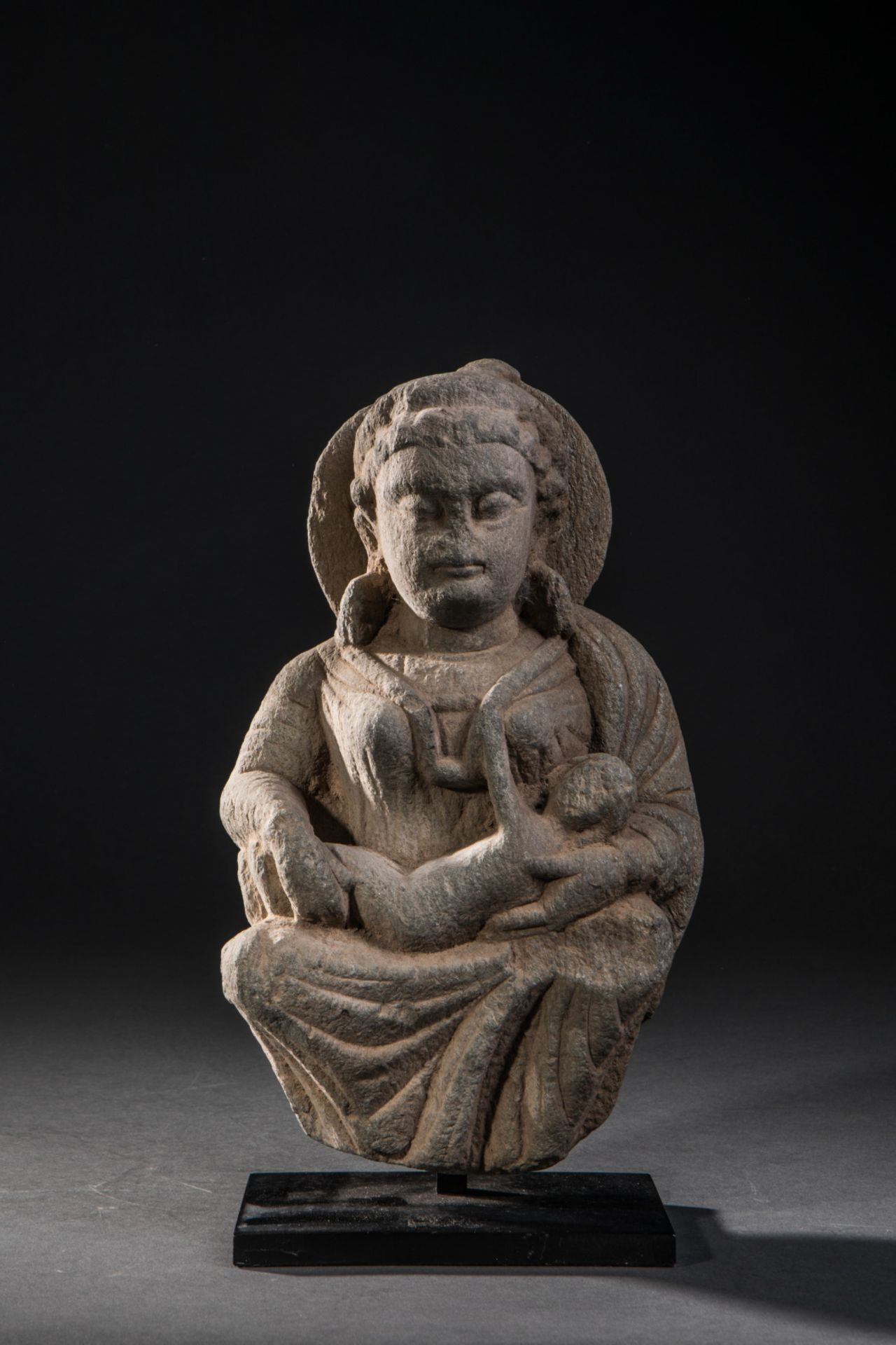 Hariti assise un enfant dans les bras, vêtue d'une robe aux plissés hellénistiques paré d'un