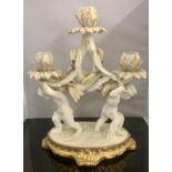 A WHITE & GILT PORCELAIN TRIO CANDLESTICK WITH CHERUBS ON BASE BY MOORE OF STOKE ON TRENT