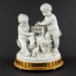 Two children with a birdcage, bisque porcelain. Signed 'Marion', early 20th C. (D:27 x W:36 x H:45 c