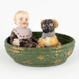 Child with a Pug, seated in a basket. Polychrome bisque porcelain. Circa 1900. (D:18 x W:24 x H:16 c