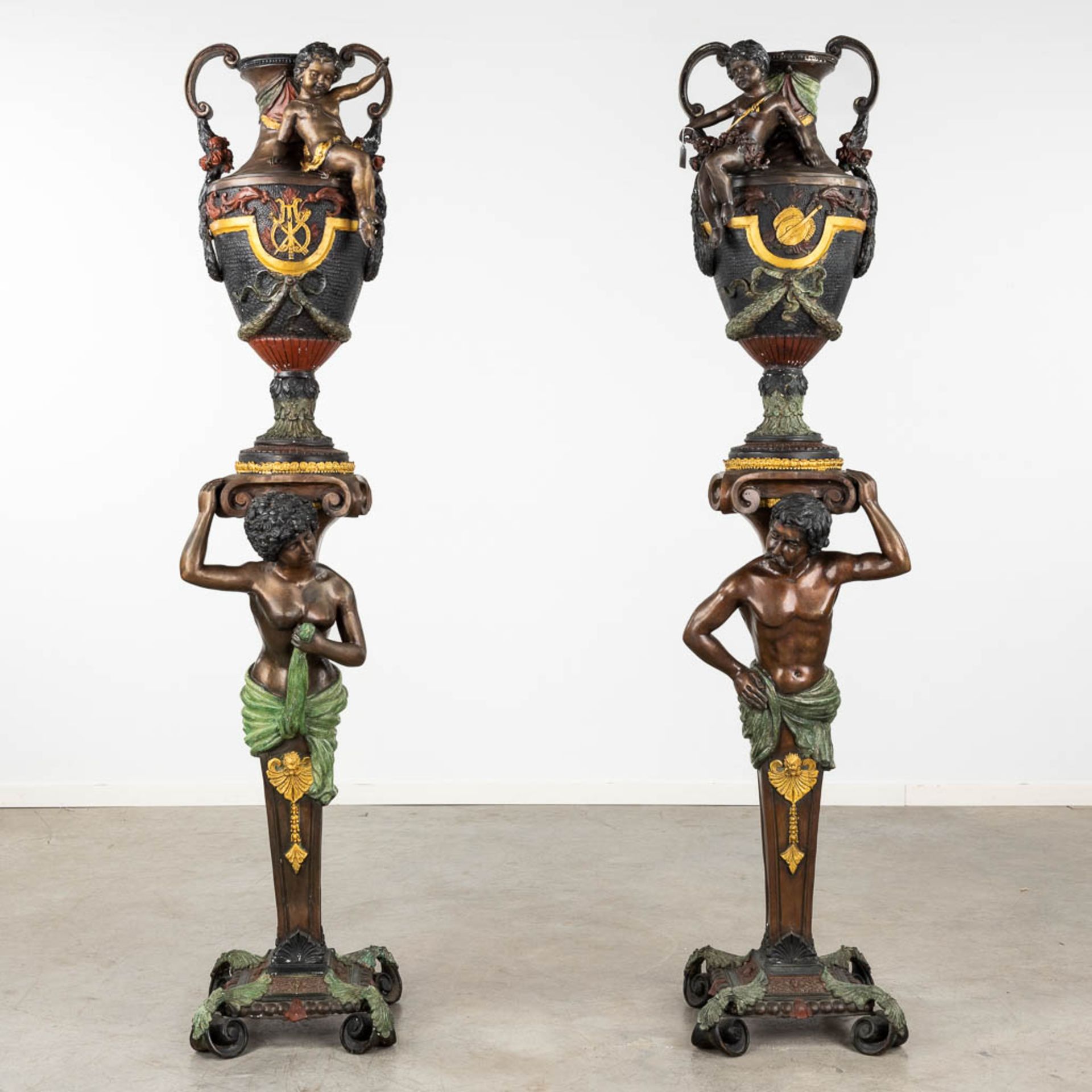 A pair of large urns standing on pedstals, decorated with figurines, bronze, 20th C. (D:38 x W:40 x 