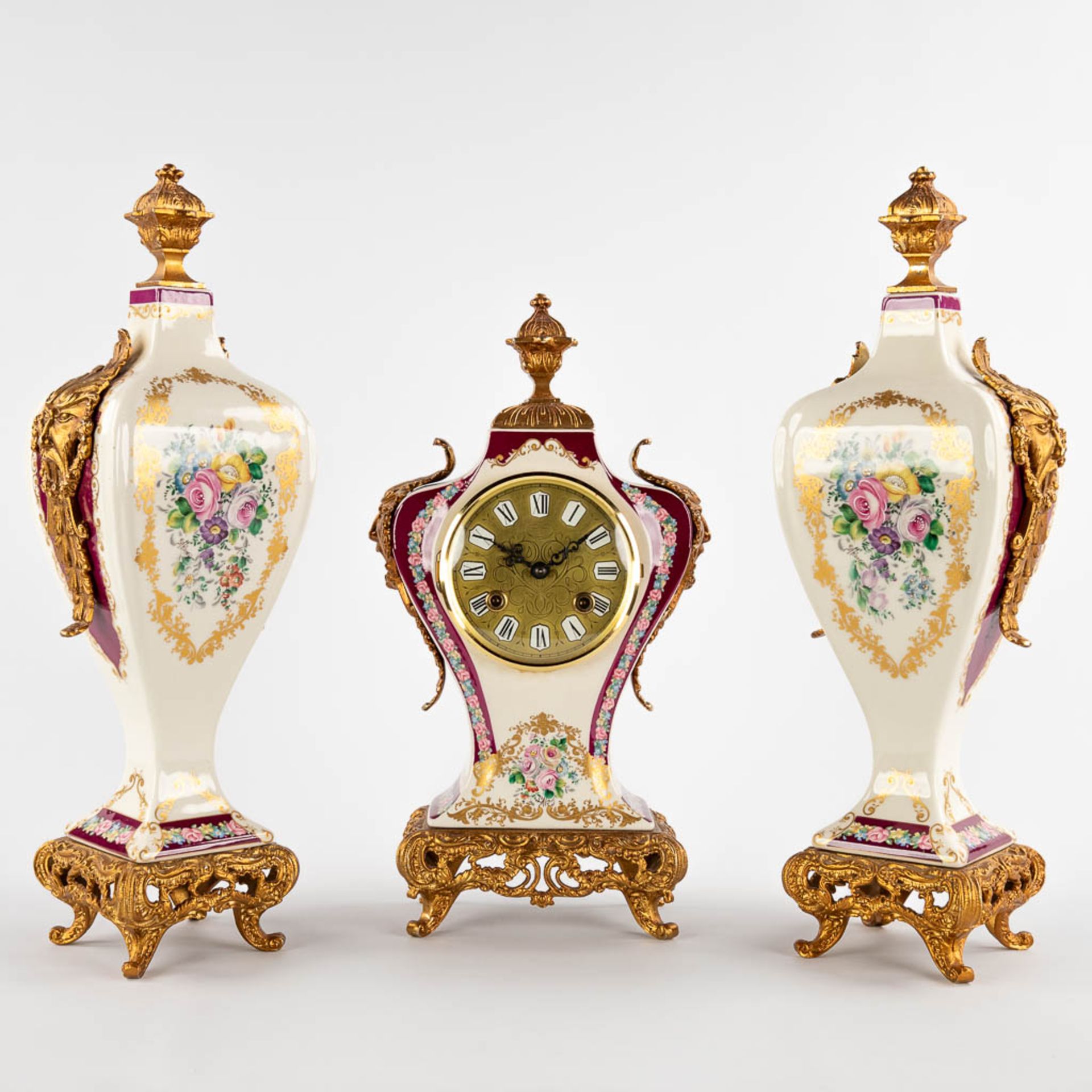 A three-piece mantle garniture clock and side pieces, porcelain mounted with bronze and floral decor
