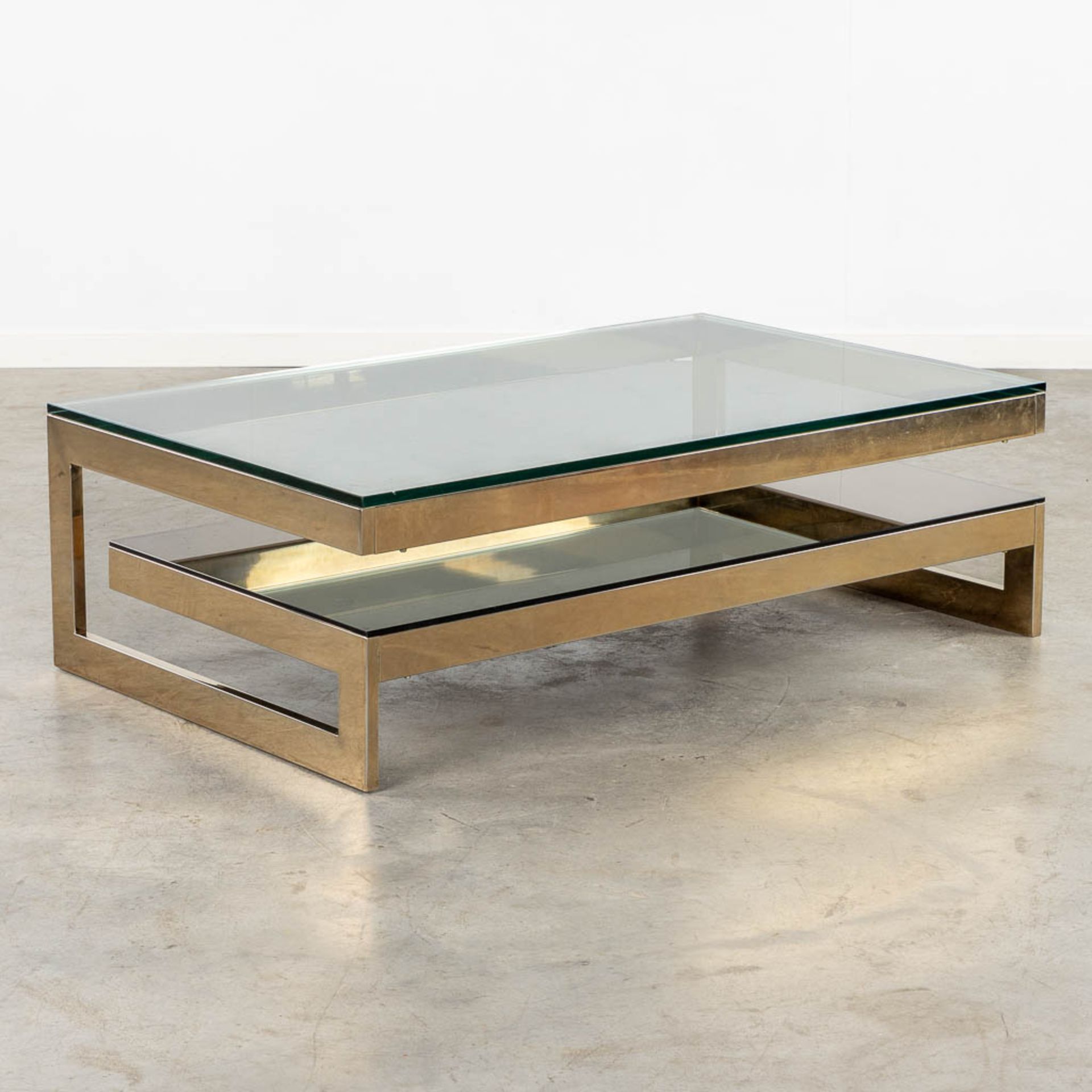Belgo Chrome, a G-shape coffee table, gilt metal and glass. (L:120 x W:75 x H:38 cm)
