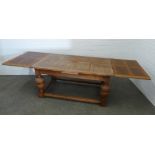 An extending oak dining table with panelled top, raised on bold cup and cover supports, united by