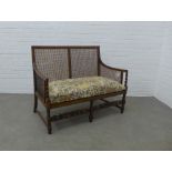 Bergère two seater settee with cane work back and sides, floral cushion and carved stretcher, . 96 x