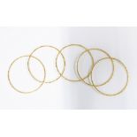 Set of five unmarked gold bangles, each with alternating textured and polished panels, likely