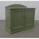 A small green cupboard with arched ledgeback and pair of panelled doors, opening to reveal a shelved