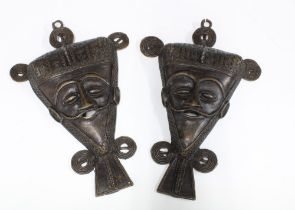 A pair of African bronze wall masks with three ringlets over a triangular face with pointed beard,