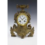 A French brass cased mantle clock, with an urn surmount over a circular dial within a rococo style