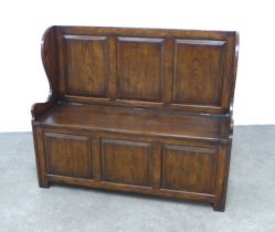 An oak monks bench, triple panelled back, lift up seat, shaped side supports and triple panelled