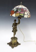 Bronze patinated figural metal table lamp base with a Tiffany style stained glass shade, 65cm