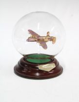 A glass model of a Lancaster Bomber, contained within a clear glass sphere, on a wooden circular