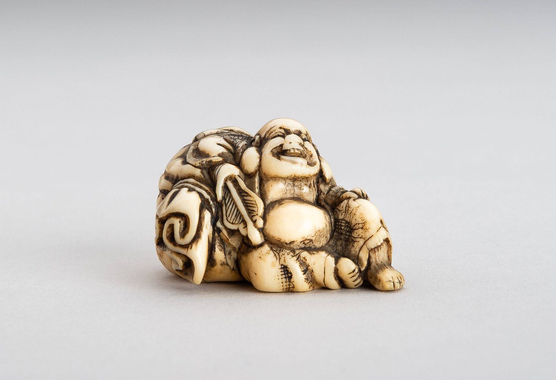 AN IVORY NETSUKE OF HOTEI WITH HIS TREASURE BAG