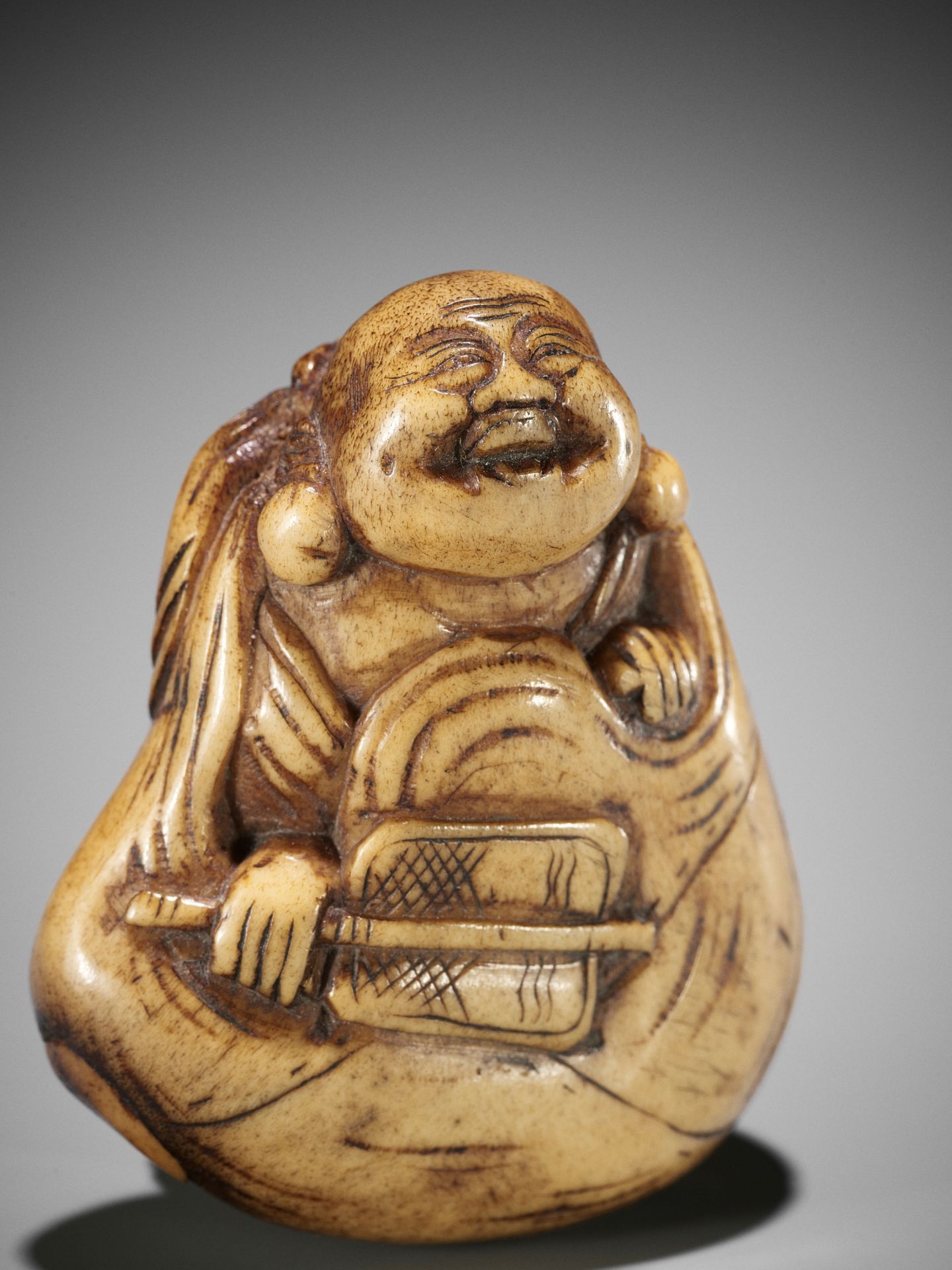 A LARGE STAG ANTLER NETSUKE OF HOTEI INSIDE HIS TREASURE BAG